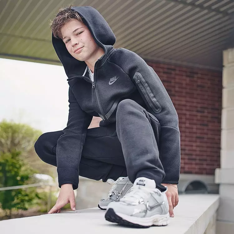 Boy posing in a dark grey Nike matching sweatsuit and silver metallic mesh athletic shoes.