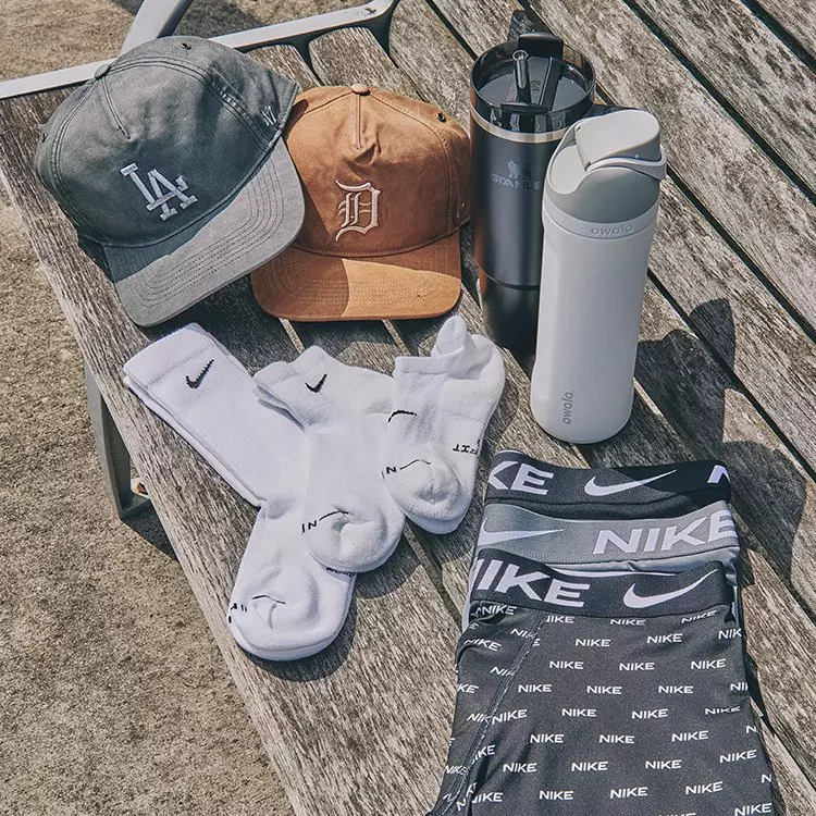 Back to school accessories on a wooden bench, including LA and Detroit baseball caps, Stanley and Owala water bottles, Nike socks, and underwear.